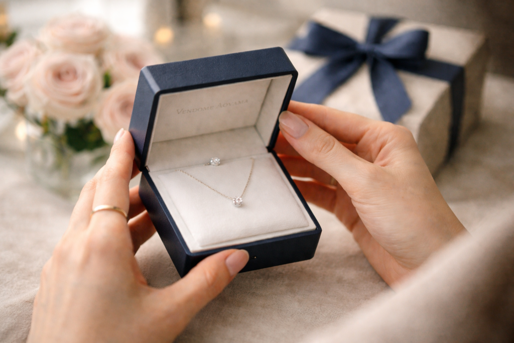 女性がネイビーのジュエリーボックスを開けて、一粒ダイヤのネックレスを見つめている横長の手元写真
